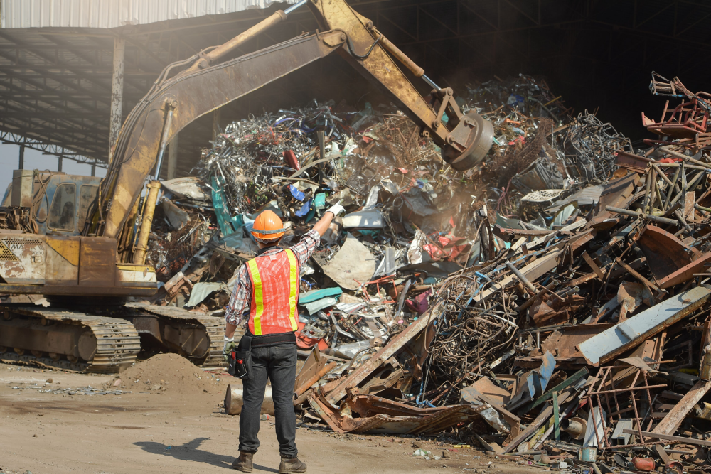 Image of a person in a construction vest and helmet standing in front of a pile of scrap metal